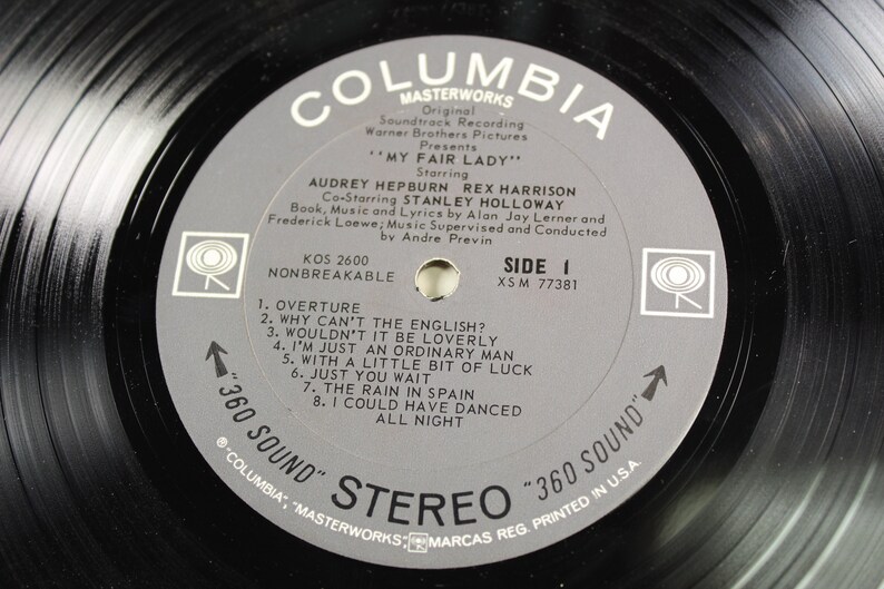 May include: A gray vinyl record with the title "My Fair Lady" starring Audrey Hepburn and Rex Harrison. The record is from Columbia Masterworks and is a 360 Sound Stereo record. The record is side one and has the song titles listed on the label.