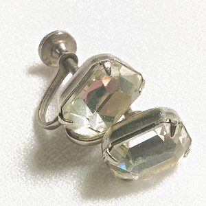 May include: A pair of silver clip-on earrings with clear iridescent stones. The stones are rectangular and have a faceted cut.