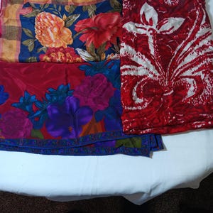 Puede incluir: Una colección de piezas de tela coloridas con estampados florales. Una pieza presenta grandes flores naranjas y rojas sobre un fondo azul oscuro. Otra tiene vibrantes flores moradas y azules sobre una base roja. Una tercera pieza es roja con un diseño floral blanco.