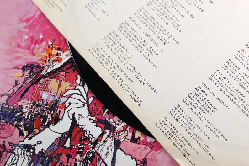May include: A vintage vinyl record with a colorful illustration of people and a car on the cover. The record is titled "Which Way America?" and includes lyrics about equality and unity. The lyrics include the phrase "What color is God's skin?"