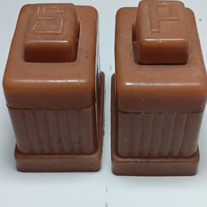 Pode incluir: Um par de saleiro e pimenteiro retangulares castanhos com detalhes canelados verticais nas laterais. Cada recipiente possui uma tampa superior quadrada com uma letra em relevo, uma marcada com um S e a outra com um P, moldados.
