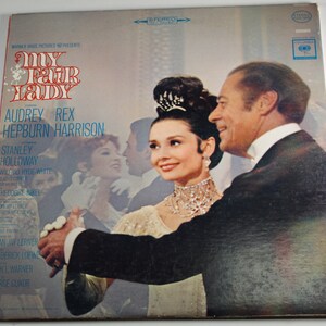 May include: A vintage vinyl record cover for the musical "My Fair Lady" starring Audrey Hepburn and Rex Harrison. The cover features a photo of Hepburn and Harrison in a ballroom scene.