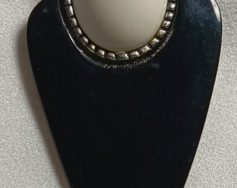 May include: A black arrow-shaped pendant with a white round cabochon stone set in a silver-toned bezel.