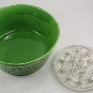 May include: A green ceramic bowl with a textured exterior and a clear glass flower frog with multiple holes. The bowl is designed to hold water and the flower frog is used to hold stems.