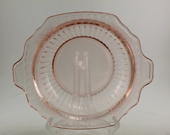 Pode incluir: Um prato de servir de vidro rosa com borda festonada e duas alças. O prato tem um design elevado e canelado.