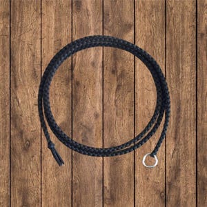 May include: A black braided rope with a silver metal ring at one end. The rope is coiled in a circle and laid on a wooden surface.