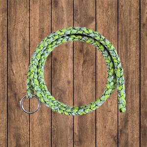 May include: A green and white braided rope with a silver ring attached. The rope is coiled in a circle and is lying on a wooden surface.