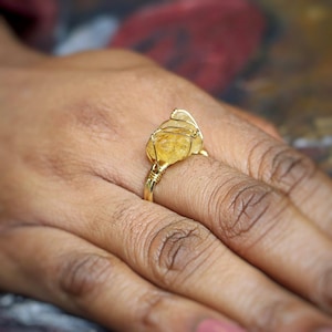 Könnte beinhalten: Ein Ring aus goldfarbenem Draht mit einem gelben Citrin-Edelstein. Der Ring wird an einem Finger getragen.