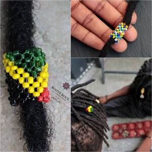 Op de afbeelding: Een close-up van een kralen dreadlock ring in de kleuren van de Jamaicaanse vlag, rood, geel en groen. De ring is gemaakt van kleine kralen en is ontworpen om op een dreadlock te worden gedragen. De ring wordt getoond op een dreadlock en in een hand.