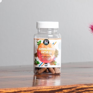 May include: A clear plastic bottle with a white lid filled with brown capsules. The label reads "Ashwagandha Capsules Healthy Stress Response" and lists benefits including "Promotes Stress Relief" and "Premium Mood Booster".