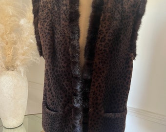 May include: A sleeveless vest with a brown leopard print pattern and dark brown fur trim. The vest has a tailored fit, with a notched collar and two front pockets. The fur trim is around the collar, armholes, and front opening.