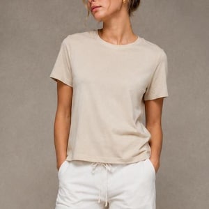 May include: A beige crew neck t-shirt and white drawstring shorts. The t-shirt has short sleeves and a relaxed fit. The shorts are high-waisted. The model is wearing gold hoop earrings.