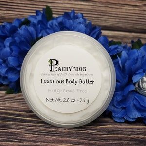 May include: A white jar of fragrance-free body butter with a label that reads "PeachyFrog Take a leap of faith towards happiness Luxurious Body Butter Fragrance Free Net Wt. 2.6 oz - 74 g".