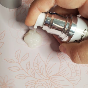 May include: A silver and white pump bottle with a clear liquid being dispensed. The bottle is labeled "D'ACHYF RCG" with the text "with hyaluronic acid" underneath.