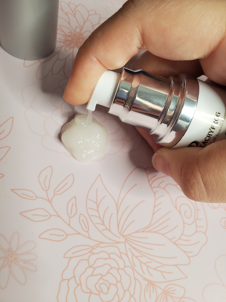 May include: A silver and white pump bottle with a clear liquid being dispensed. The bottle is labeled "D'ACHYF RCG" with the text "with hyaluronic acid" underneath.