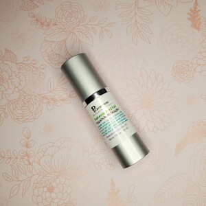 May include: A silver bottle of Peach & Bog "Hyduronic Acid Gel" skin care product. The bottle is labeled with the product name and ingredients. The bottle is on a pink background with a floral pattern.