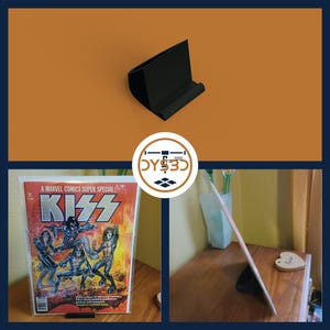 May include: Black plastic stand for displaying comic books or other items. The stand is shown holding a comic book with a KISS cover. The comic book cover features a red and yellow KISS logo with the band members in a fiery background.