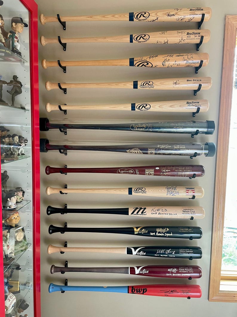 K&ouml;nnte beinhalten: Eine Wandmontage von 12 Baseballschl&auml;gern, alle von verschiedenen Spielern signiert. Die Schl&auml;ger sind vertikal angeordnet, wobei der oberste Schl&auml;ger der &auml;lteste und der unterste Schl&auml;ger der neueste ist. Die Schl&auml;ger sind alle in verschiedenen Farben und haben verschiedene Logos und Inschriften. Die Schl&auml;ger sind alle in gutem Zustand und eine gro&szlig;artige Erg&auml;nzung f&uuml;r jede Baseball-Sammlung.