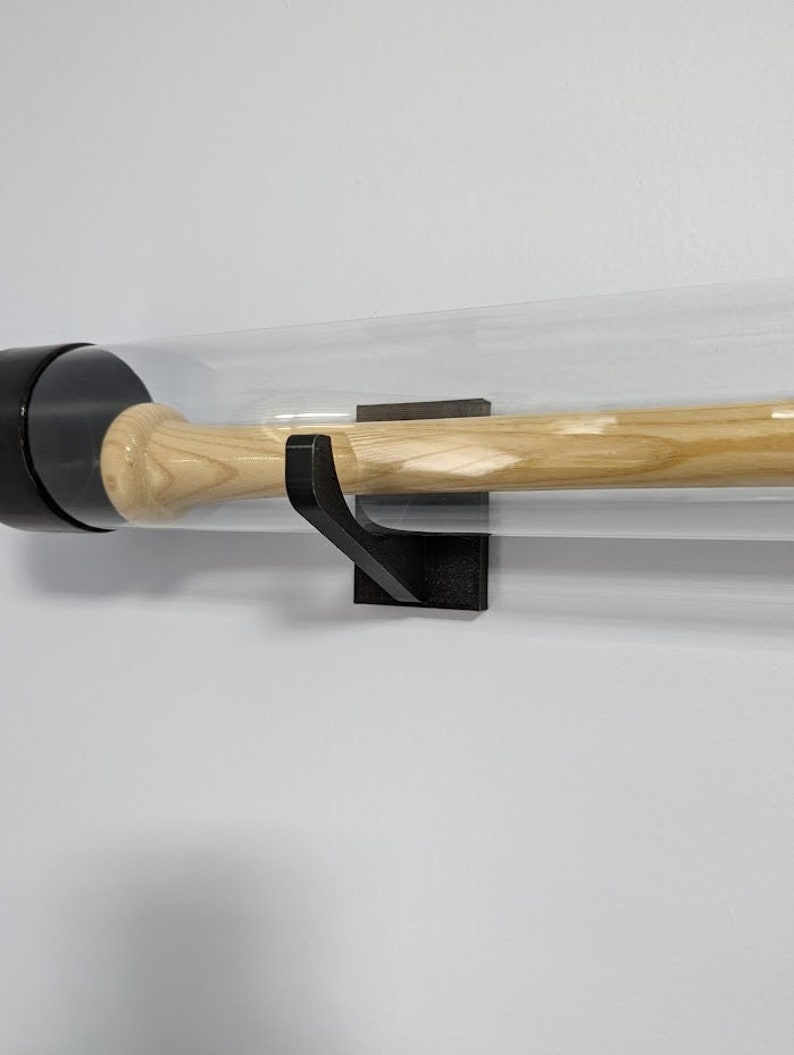 K&ouml;nnte beinhalten: Ein schwarzer Baseballschl&auml;gerhalter mit einem durchsichtigen Acrylrohr zur Pr&auml;sentation eines Baseballschl&auml;gers. Der Halter ist an einer wei&szlig;en Wand montiert.