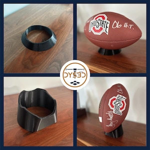May include: Three 3D printed black football display stands. The stands are designed to hold a football upright. The stands are shown on a wooden surface.