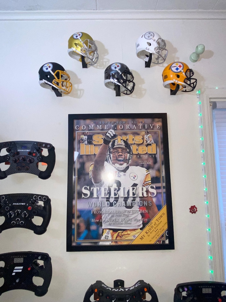 May include: A framed magazine cover featuring a football player in a black and yellow uniform with the text "Steelers World Champions" and "Super Bowl XL Commemorative".  The image also shows six football helmets in black, white, and gold with the Pittsburgh Steelers logo.