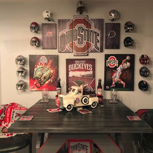May include: A room decorated with Ohio State Buckeyes memorabilia, including framed prints, football helmets, and a toy pickup truck. The room also features a wooden table with coasters and a blanket with the Ohio State logo.