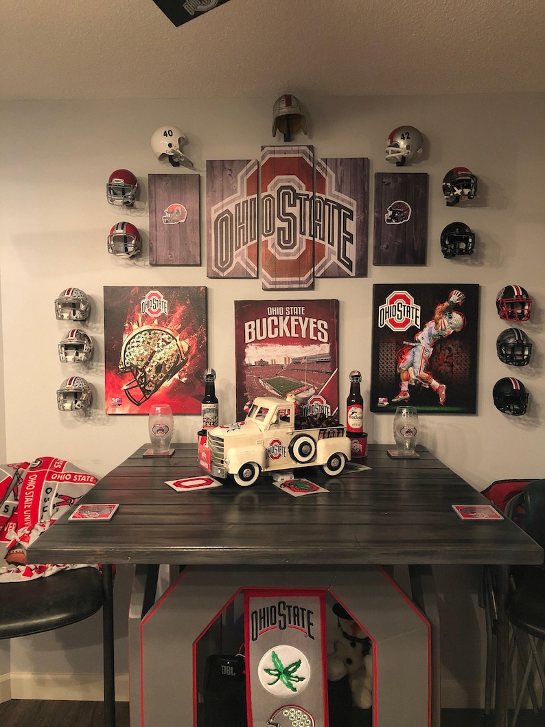 May include: A room decorated with Ohio State Buckeyes memorabilia, including framed prints, football helmets, and a toy pickup truck. The room also features a wooden table with coasters and a blanket with the Ohio State logo.
