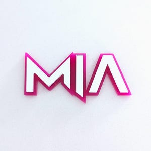 Può includere: Un ritaglio acrilico rosa e bianco con il nome "MIA". Le lettere sono bianche con un contorno rosa, creando un effetto a strati. Il design è moderno e pulito, adatto a varie applicazioni.