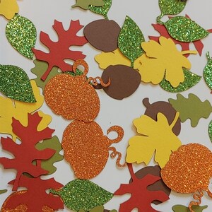 Puede incluir: Surtido de confeti de temática otoñal con calabazas con purpurina, hojas y bellotas en tonos naranja, rojo, verde, marrón y amarillo.