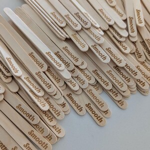 May include: A pile of light-coloured wooden craft sticks, each engraved with the word "Smooth". The sticks are arranged in a slightly overlapping pattern, creating a textured surface. The overall effect is a natural, neutral aesthetic.