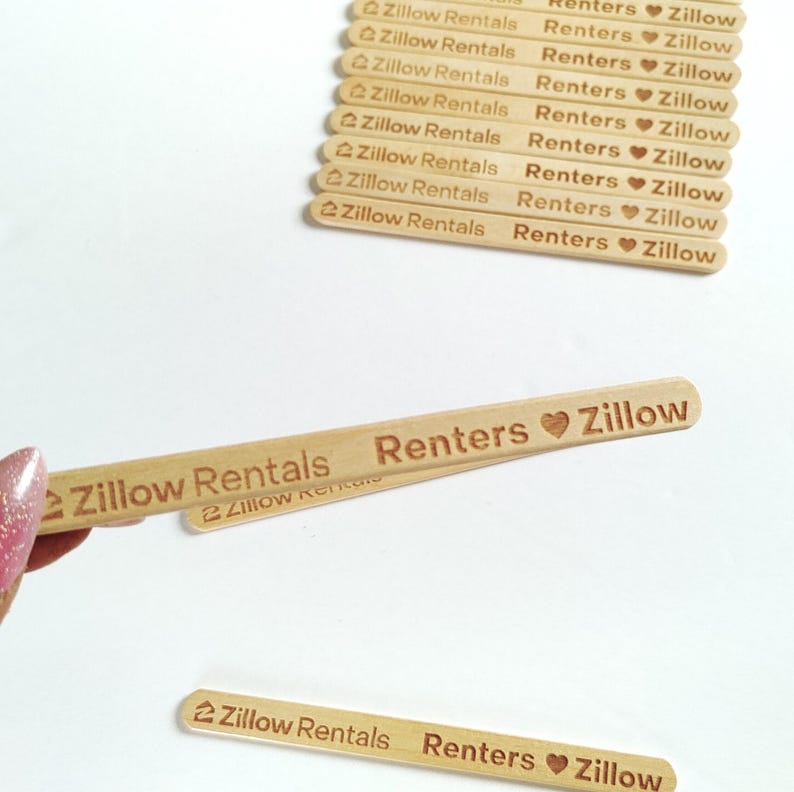May include: Wooden craft sticks with the text "Zillow Rentals Renters Zillow" in a brown font. The sticks have rounded ends and a heart symbol. A hand holds one stick, with others in the background.