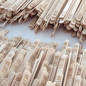 May include: A close-up of numerous light-coloured wooden craft sticks, each bearing the word "CALLAB". The sticks are piled together, indicating their use in crafts or similar activities.