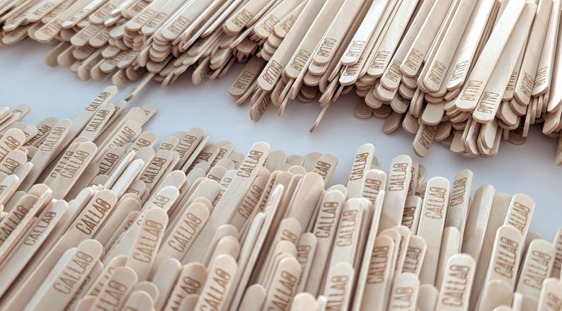 May include: A close-up of numerous light-coloured wooden craft sticks, each bearing the word "CALLAB". The sticks are piled together, indicating their use in crafts or similar activities.
