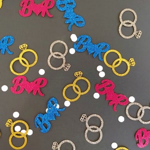 Può includere: Assortimento di coriandoli glitterati in varie forme e colori, tra cui anelli, cuori e la parola "Bride".
