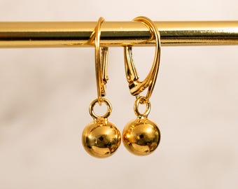 May include: A pair of gold dangle earrings with a round ball charm at the end of each earring.