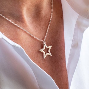May include: A silver necklace with a large, open star pendant. The star is hollow and has a slightly textured surface.