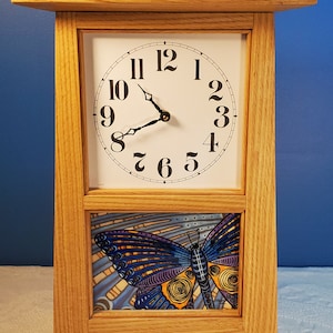 May include: A wooden clock with a white face and black hands. The clock has a butterfly design on the bottom. The clock is 12 inches tall.