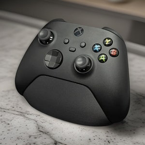 Peut inclure: Une manette Xbox Series X noire avec une poignée texturée et un pavé directionnel noir et blanc. La manette a une disposition de boutons noir et blanc avec les lettres A, B, X et Y.