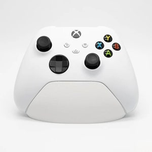 Peut inclure: Une manette sans fil Xbox blanche avec des boutons noirs et un pavé directionnel noir. La manette a une surface texturée et un logo Xbox blanc sur le devant.