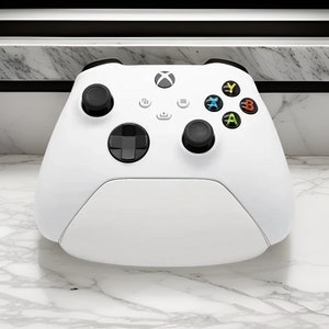 Peut inclure: Une manette Xbox Series X blanche avec des boutons noirs et un pavé directionnel noir. La manette a un logo Xbox blanc sur le devant.