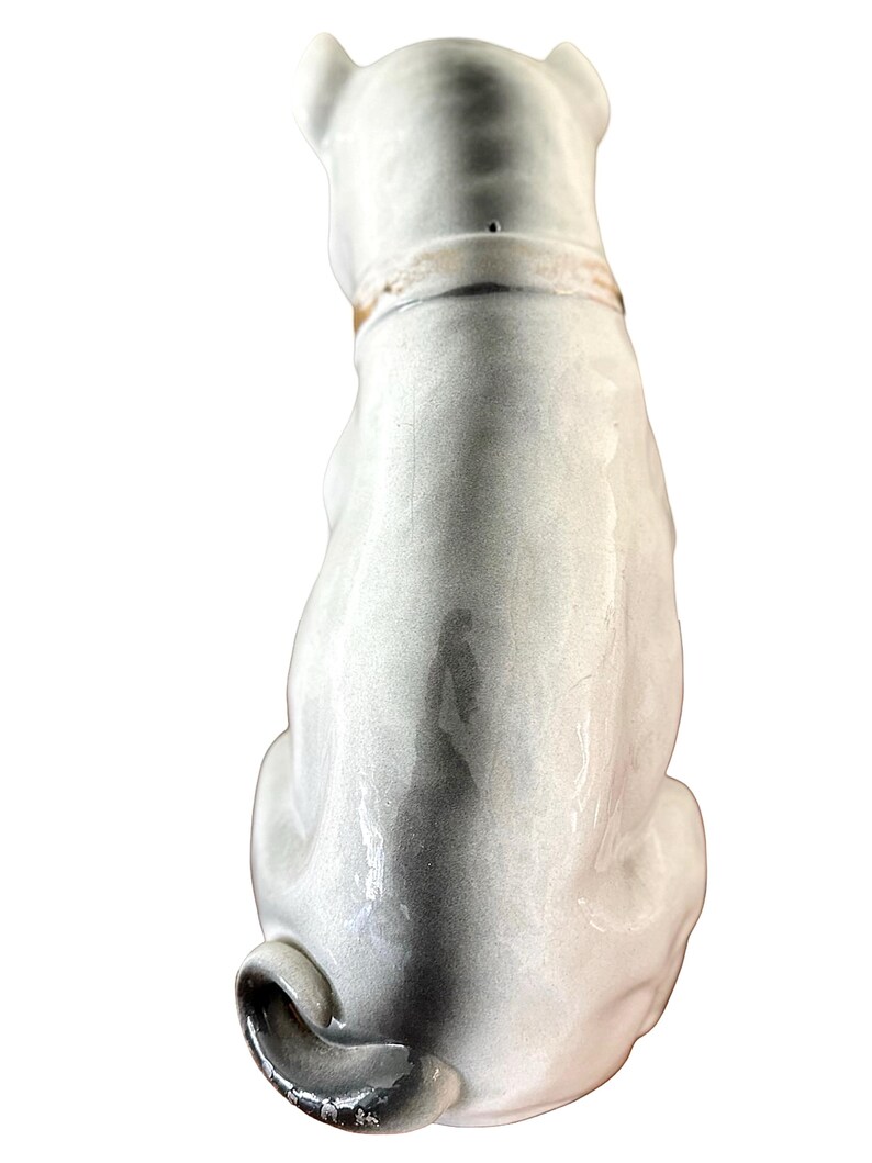 May include: A ceramic dog figurine, viewed from the back, in shades of gray and white. The dog is seated with its tail curled. It has a collar around its neck. The figurine has a glossy finish.