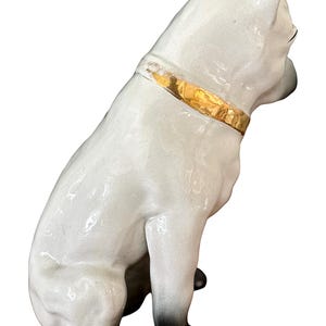 May include: A ceramic dog figurine in a seated position, with a glossy white finish and black paws. The dog wears a gold-colored collar. The figurine is a decorative item.