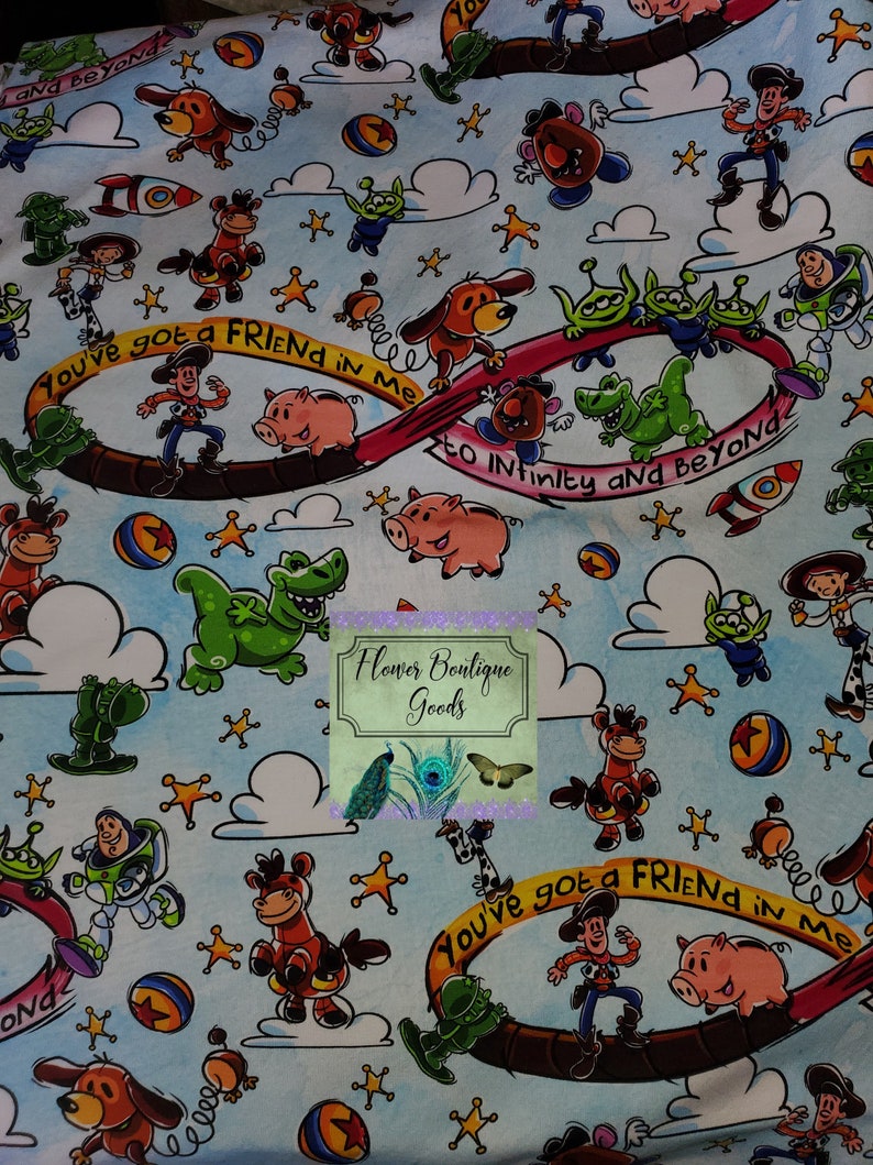 May include: A blue and white fabric with a repeating pattern of Toy Story characters, including Woody, Buzz Lightyear, Rex, and the alien trio. The fabric features the phrase "You've got a friend in me" and "To infinity and beyond".