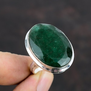 May include: A silver ring with a large, oval-shaped emerald green gemstone.
