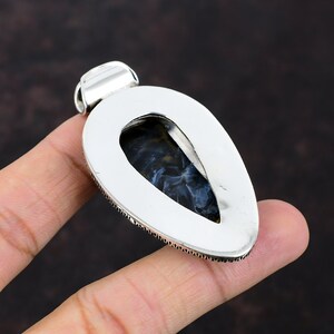 Pu&ograve; includere: Ciondolo in argento con una pietra di occhio di tigre blu a forma di lacrima incastonata in una cornice d'argento. Il ciondolo ha un bordo dettagliato e un'anellina per attaccare una catena.