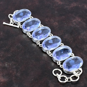 Può includere: Un bracciale in argento con sei pietre preziose ovali blu chiaro. Le pietre sono incastonate in castoni individuali in argento e collegate da maglie a catena in argento. Chiusura a toggle.