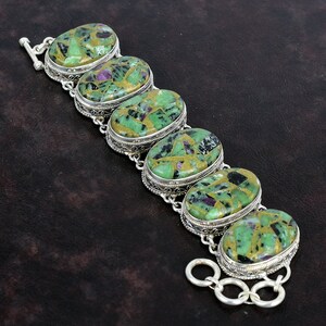 Può includere: Un braccialetto d'argento con sette pietre ovali di colore verde, nero e rosa. Il braccialetto ha una chiusura a scatto.
