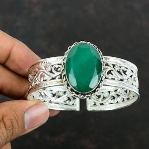 May include: A silver cuff bracelet with an oval-shaped green gemstone set in a filigree design.
