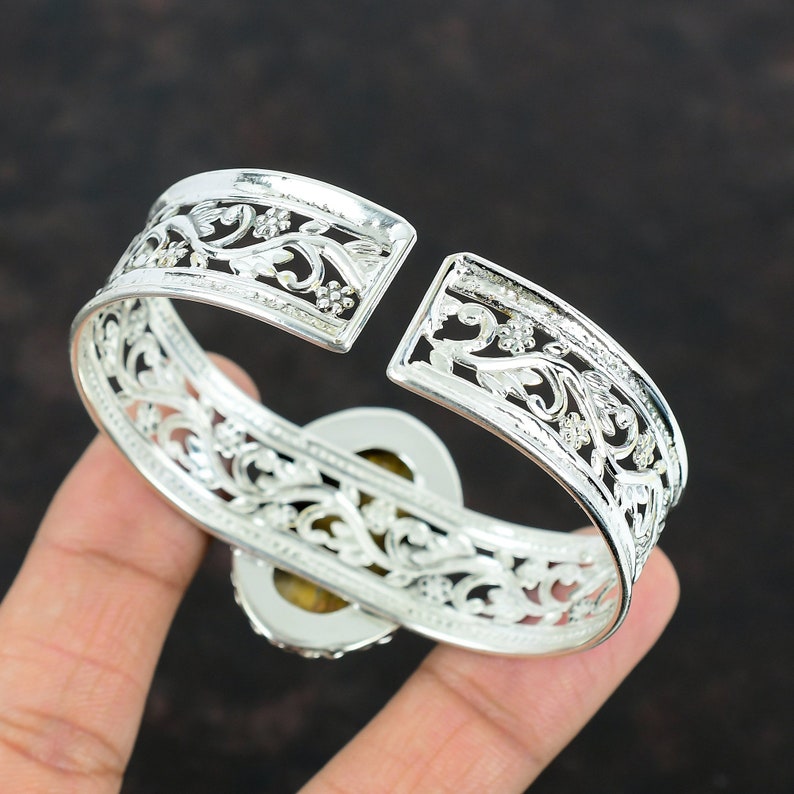 May include: Silver bangle bracelet with an intricate floral design and a large oval gemstone in the center.