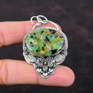 Pode incluir: Um pingente de prata com uma gema verde, dourada e preta engastada em um design floral.